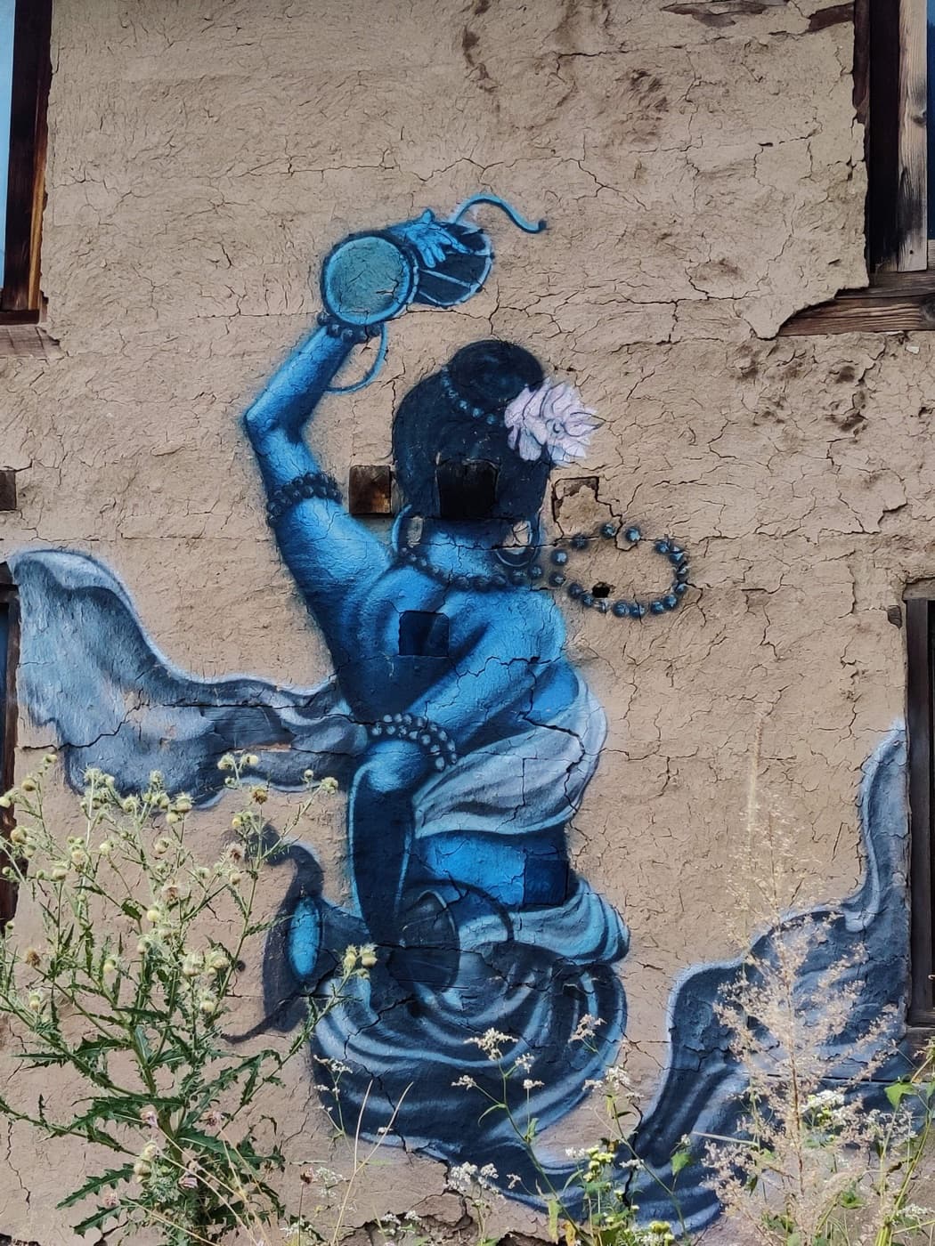 Blue mural of a dancing figure on a weathered wall